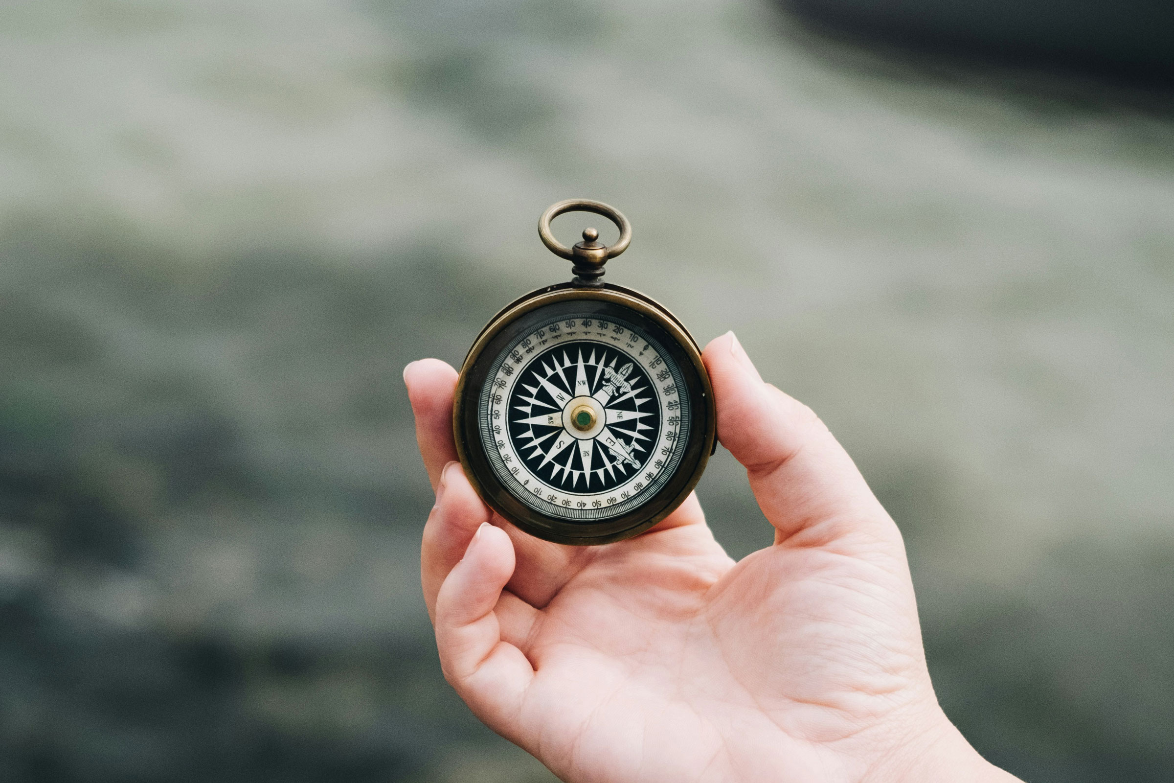 Eine Hand hält einen alt anmutenden Kompass in der Hand